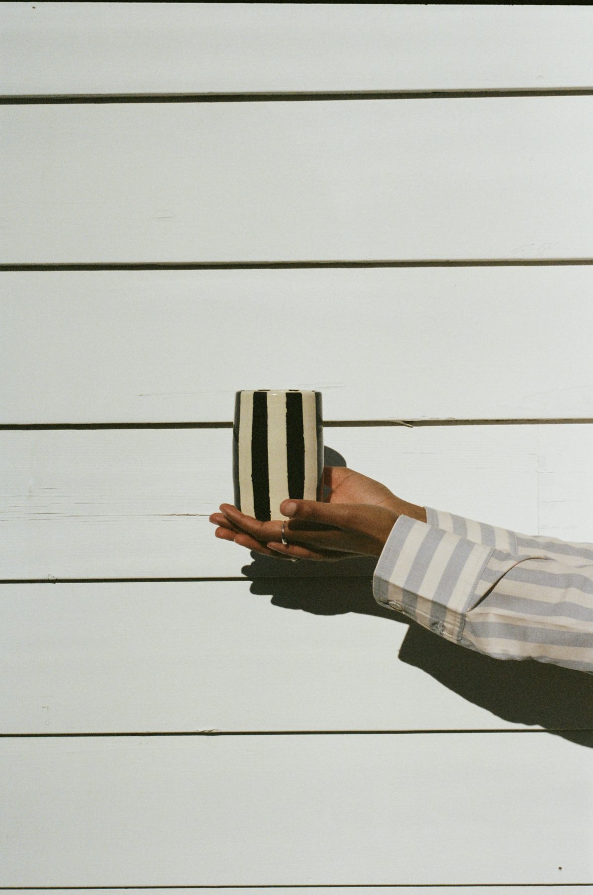 Holding a hand-striped ceramic cup in the sun